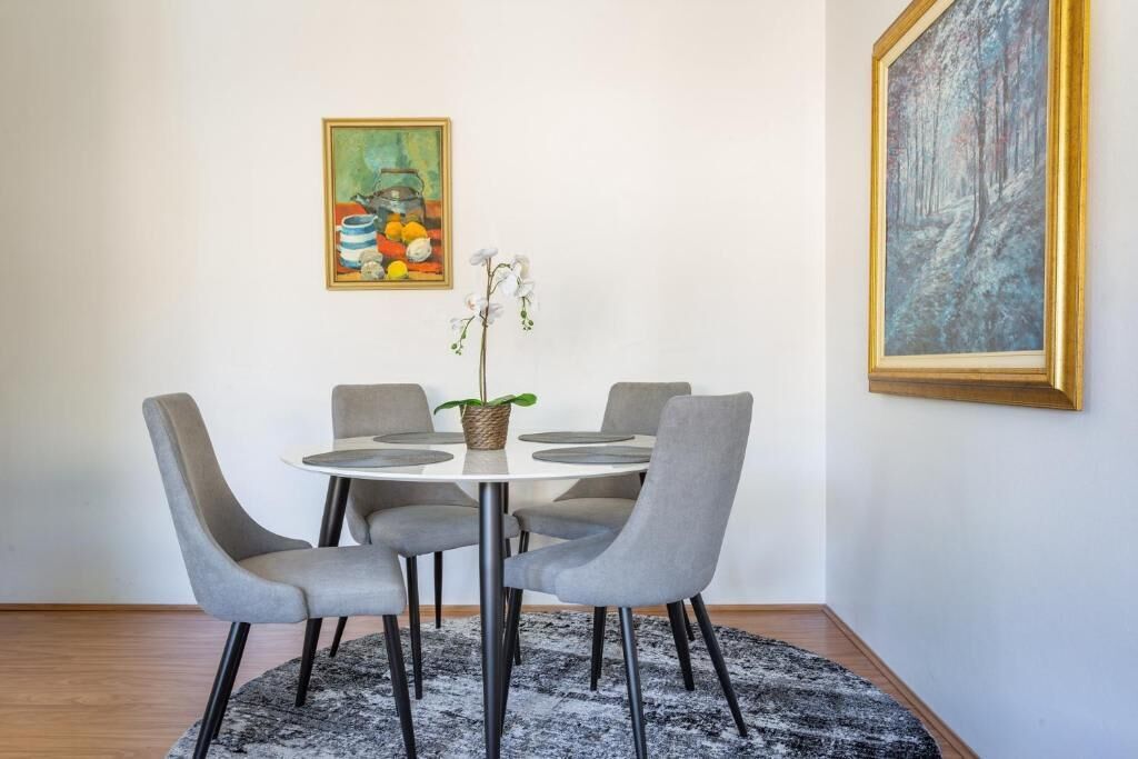 Un coin repas avec une table ronde, quatre chaises grises, une plante en pot et deux œuvres d’art encadrées accrochées au mur.