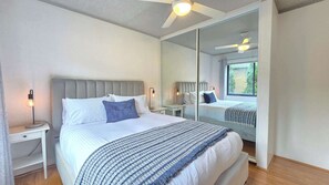 Un dormitorio moderno con una cama grande, mesitas de noche, un ventilador de techo y un espejo grande que refleja la habitación.
