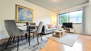 A living room with a dining area, a sofa, a television, and a painting on the wall. - Refined comfort 1 bed Neutral Bay w parking & balcony (Neutral Bay)