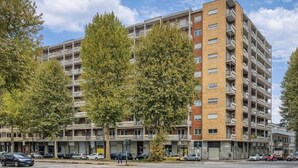 Un edificio de apartamentos de varios pisos con balcones, estacionamiento y árboles.