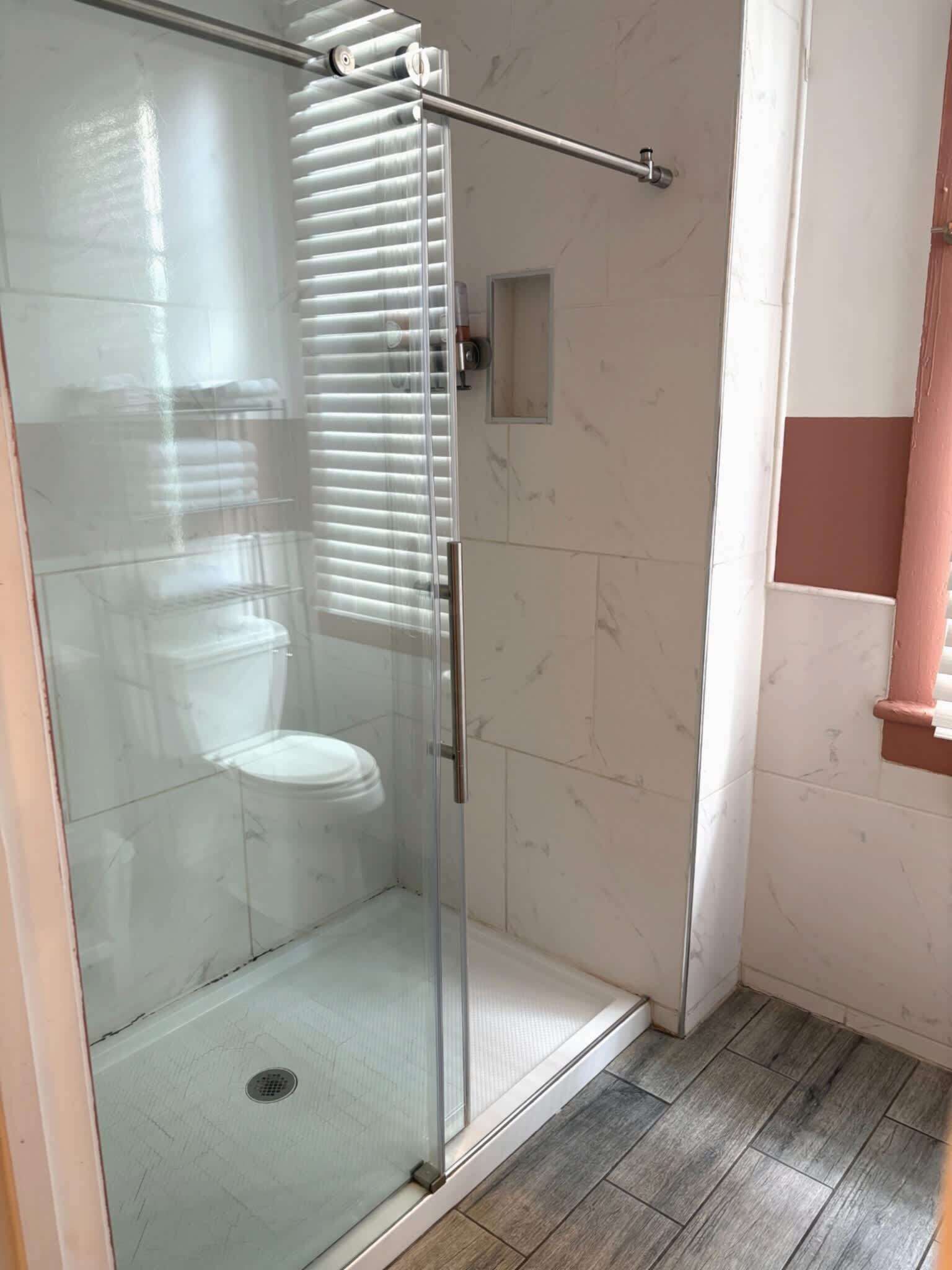Une cabine de douche fermée par des parois en verre, avec des toilettes, un petit miroir et un porte-serviettes.