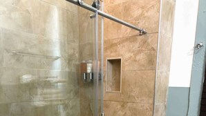 A glass-enclosed shower stall with a metal handle, a toilet, and a small shelf with toiletries. - 3BR Gem Near Garden District (New Orleans)