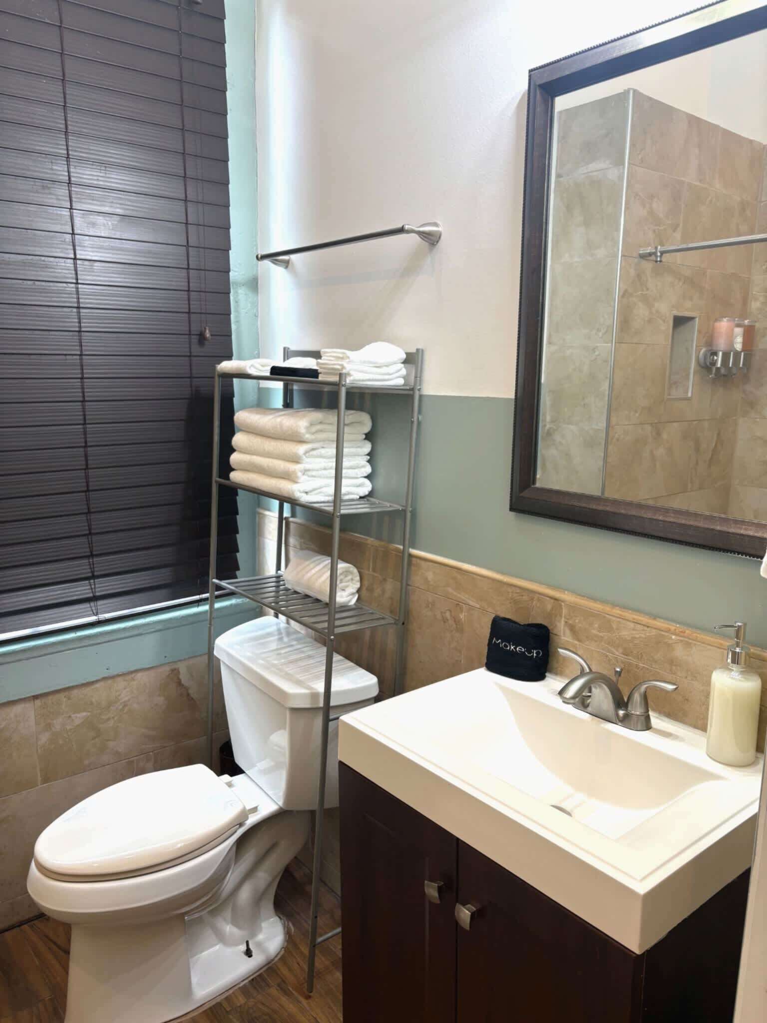 A bathroom with a toilet, a sink, a mirror, and a towel rack with folded towels.