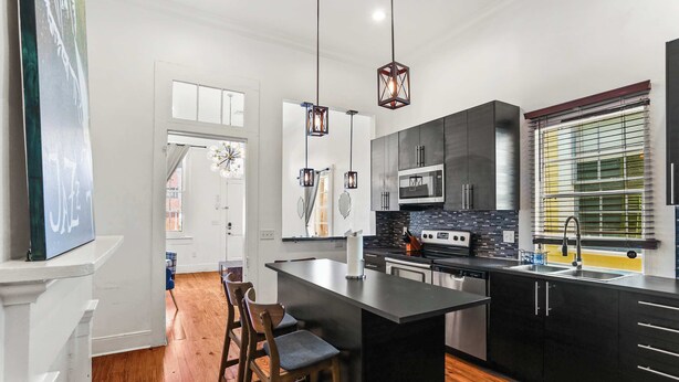A modern kitchen with a central island, dark cabinetry, and pendant lighting. - 3BR Gem Near Garden District (New Orleans)