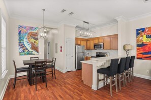 Una cocina moderna con armarios de madera, una isla central con taburetes y una zona de comedor con mesa y sillas de madera.