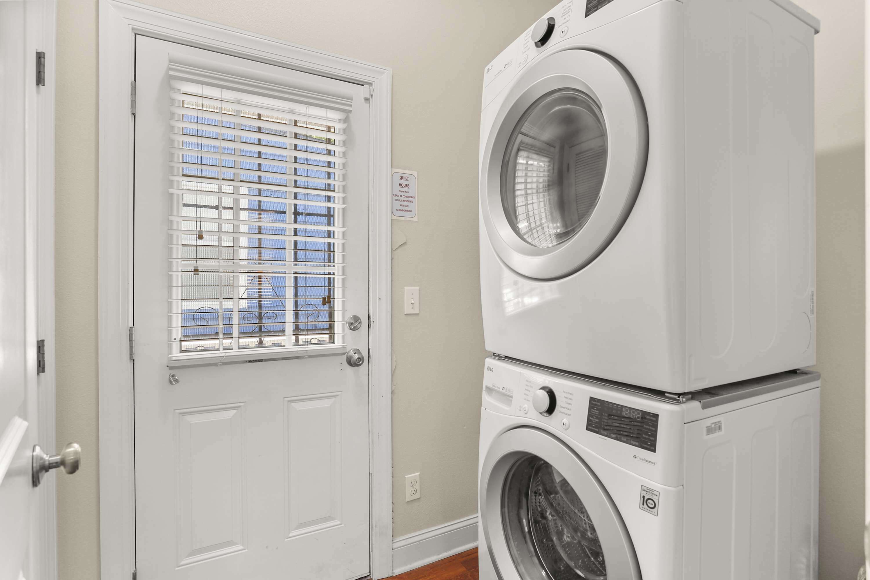 Une buanderie équipée de machines à laver et de sèche-linge superposés, une porte avec une fenêtre et un panneau indiquant la fonction de la pièce.