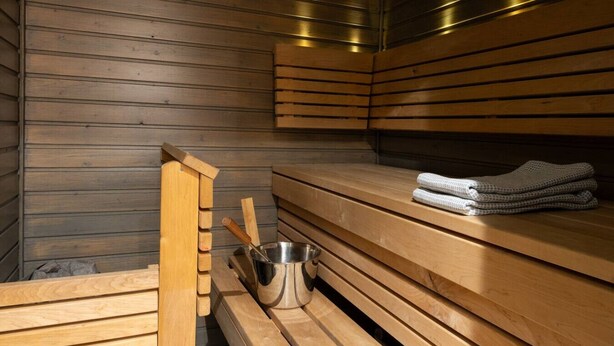 Eine Sauna mit Holzbänken, einem Metallkübel und Handtüchern.