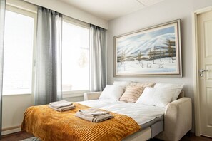 A bedroom with a bed, a window with curtains, a painting on the wall, and a door. - Cozy City Apartment with Private Sauna and Parking (Rovaniemi)