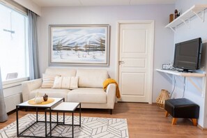 A living room with a sofa, a coffee table, a TV, and a painting. - Cozy City Apartment with Private Sauna and Parking (Rovaniemi)