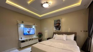 A modern hotel room with a large bed, a flat-screen TV, a bedside table, and a ceiling light. - VENUS HOTEL (Onitsha)