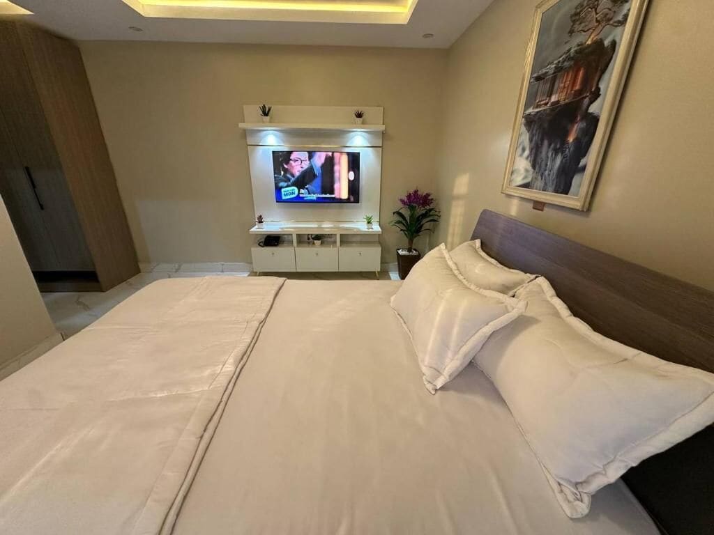 A hotel room with a large bed, a TV mounted on a cabinet, and a painting on the wall.