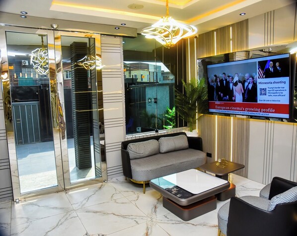 A modern lobby with a sofa, coffee table, and a TV displaying news.