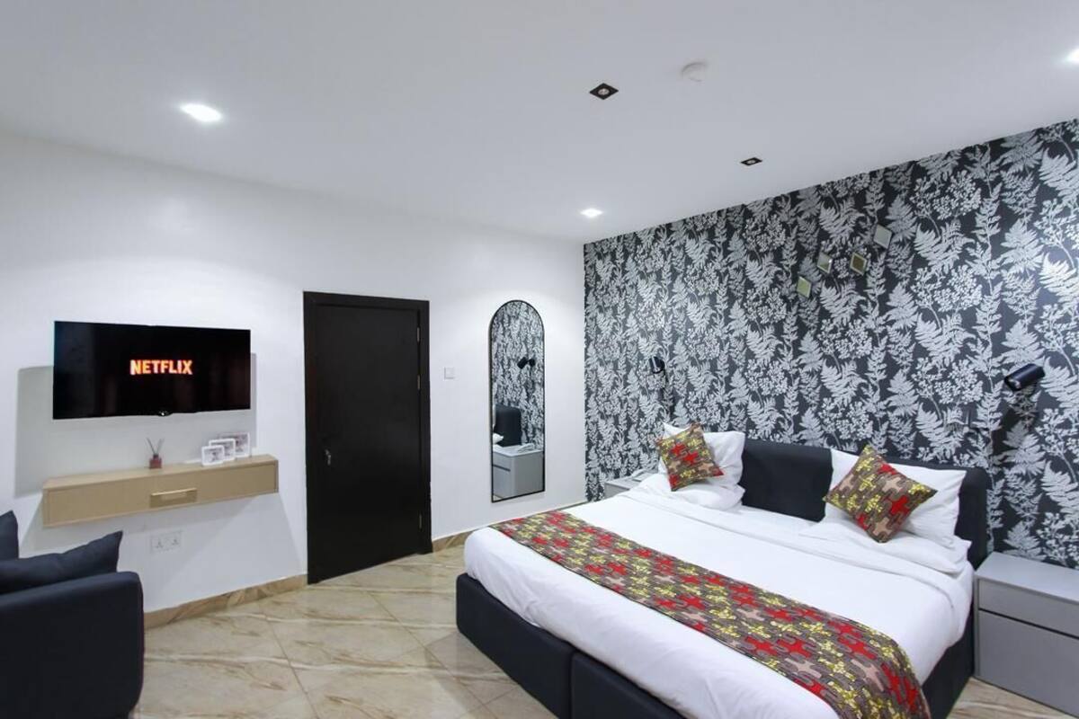 A modern hotel room with a large bed, a TV mounted on the wall, a bedside table, and a patterned wallpaper.