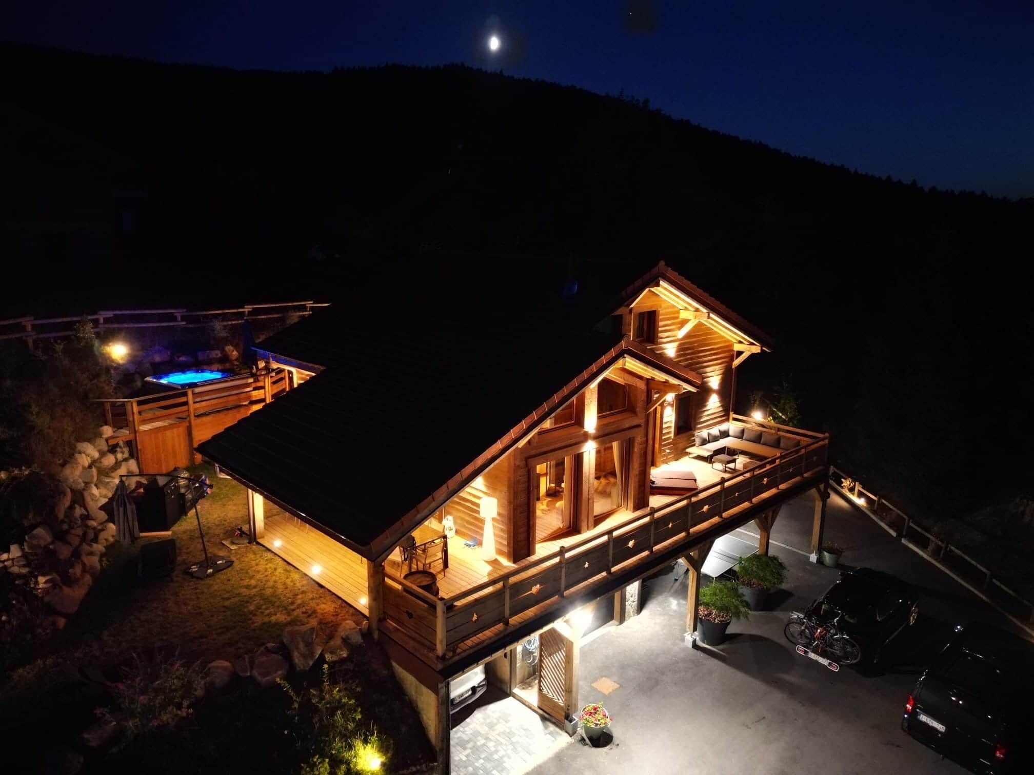 A two-story wooden cabin with a balcony, a swimming pool, and a car parked in the driveway.