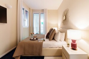 Ein Hotelzimmer mit Bett, Nachttisch, Lampe und Blick ins Freie durch ein Fenster.