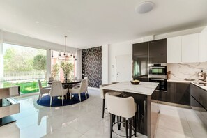 A modern kitchen with a dining area, large windows, and a view of greenery. - Villa Olmo Luxury Suites - Suite Nobile (Como)