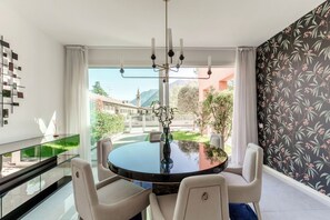 Ein Essbereich mit einem runden Tisch, Stühlen, einer Chandelierleuchtre und Blick auf Gebäude und Grünflächen.