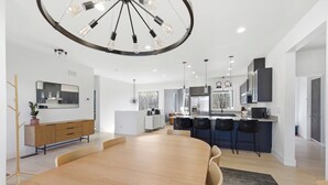 A modern kitchen with a central island, pendant lighting, and a large dining table.