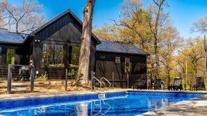 A pool area with a wooden building, a tree, and a clear blue sky.