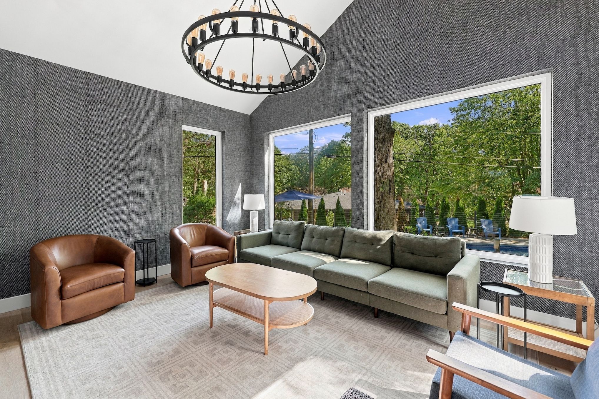 Un salon moderne comprenant un canapé, des fauteuils, une table basse et une grande fenêtre donnant sur un paysage verdoyant.