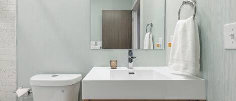Une salle de bain avec des toilettes blanches, un lavabo surmonté d’un miroir et une serviette suspendue à un anneau en métal.