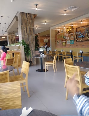 Un restaurante con sillas y mesas de madera, una barra donde una persona atiende, y una pared decorada con diversos objetos, incluyendo una bicicleta.