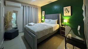 A bedroom with a bed, bedside tables, a chair, an air conditioning unit, and a view of the outside. - Sunset Place One Bedroom in Front of Pucmm (Santiago de los Caballeros)