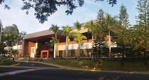 A modern building with a large entrance, palm trees, and a clear sky. - Sunset Place One Bedroom in Front of Pucmm (Santiago de los Caballeros)