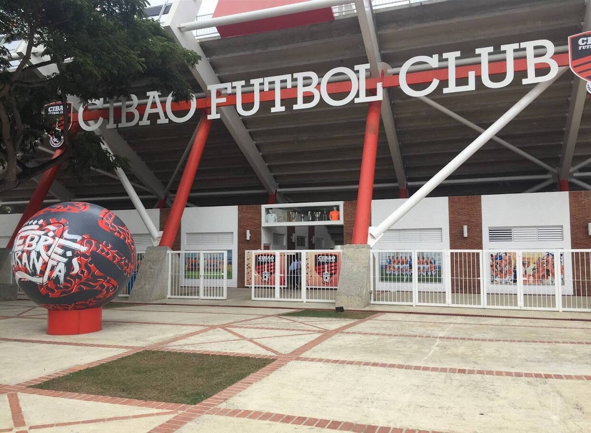 A sports facility with a prominent sign reading 'CIBAO FUTBOL CLUB' and a large decorative sphere in the foreground.