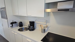 A modern kitchen with white cabinets, a black stove, a coffee maker, and a kettle. - Newly renovated vacation home in a quiet park. Fully fenced garden. (Callantsoog)