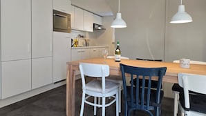 A modern kitchen with white cabinets, a wooden dining table, and two pendant lights. - Newly renovated vacation home in a quiet park. Fully fenced garden. (Callantsoog)