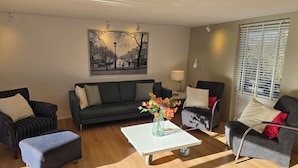 A modern living room with a sofa, armchairs, a coffee table, and a painting on the wall. - Newly renovated vacation home in a quiet park. Fully fenced garden. (Callantsoog)
