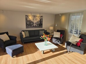 A modern living room with a sofa, armchairs, a coffee table, and a painting on the wall. - Newly renovated vacation home in a quiet park. Fully fenced garden. (Callantsoog)