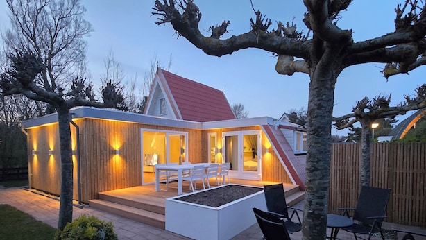 A modern house with a red roof, a patio with chairs, and a wooden deck. - Newly renovated vacation home in a quiet park. Fully fenced garden. (Callantsoog)