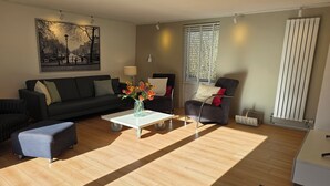 A living room with a sofa, armchair, coffee table, and a painting on the wall. - Newly renovated vacation home in a quiet park. Fully fenced garden. (Callantsoog)
