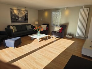 A living room with a sofa, armchair, coffee table, and a painting on the wall. - Newly renovated vacation home in a quiet park. Fully fenced garden. (Callantsoog)