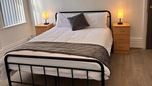 A neatly made bed with a metal frame, two bedside tables with lamps, and a window with blinds. - Near Beach - Parking - Wifi - Sleeps 2 (Lytham St. Anne's)