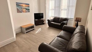 A living room with a brown leather sofa, a TV stand, a bench, and a painting on the wall. - Near Beach - Parking - Wifi - Sleeps 2 (Lytham St. Anne's)