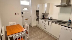 A compact kitchen with a wooden table and chairs, a built-in oven, a toaster, and a dishwasher. - Near Beach - Parking - Wifi - Sleeps 2 (Lytham St. Anne's)