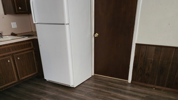 A kitchen with a white refrigerator, wooden cabinets, and a brown door. - Nice 3-bedroom house with AC in peaceful Lubbock neighborhood (Lubbock)