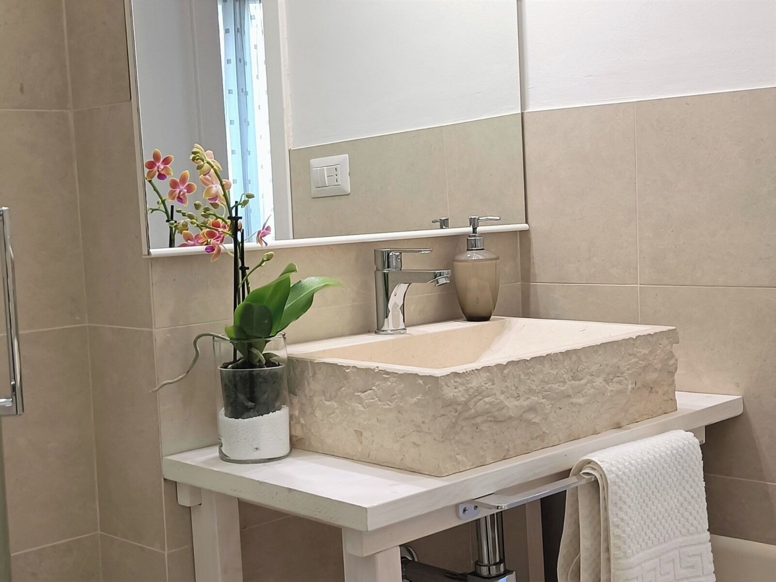 Een badkamer met een groot, rechthoekig wastafelblad, een spiegel erboven en een potorkidee op het aanrecht.