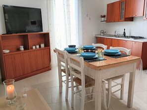 A compact kitchen with wooden cabinets, a dining table set with blue plates and glasses, and a TV on a stand. - Casa Fla Il ponte sul Salento Appartamento a pochi chilometri da Lecce (Trepuzzi)