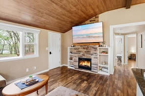 Una sala de estar con chimenea, pisos de madera, televisor y vistas al exterior.