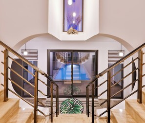 Ein modernes Interieur mit einer Treppe, die zu einer Glastür führt, Blick auf einen Pool und einer Zierpflanze.