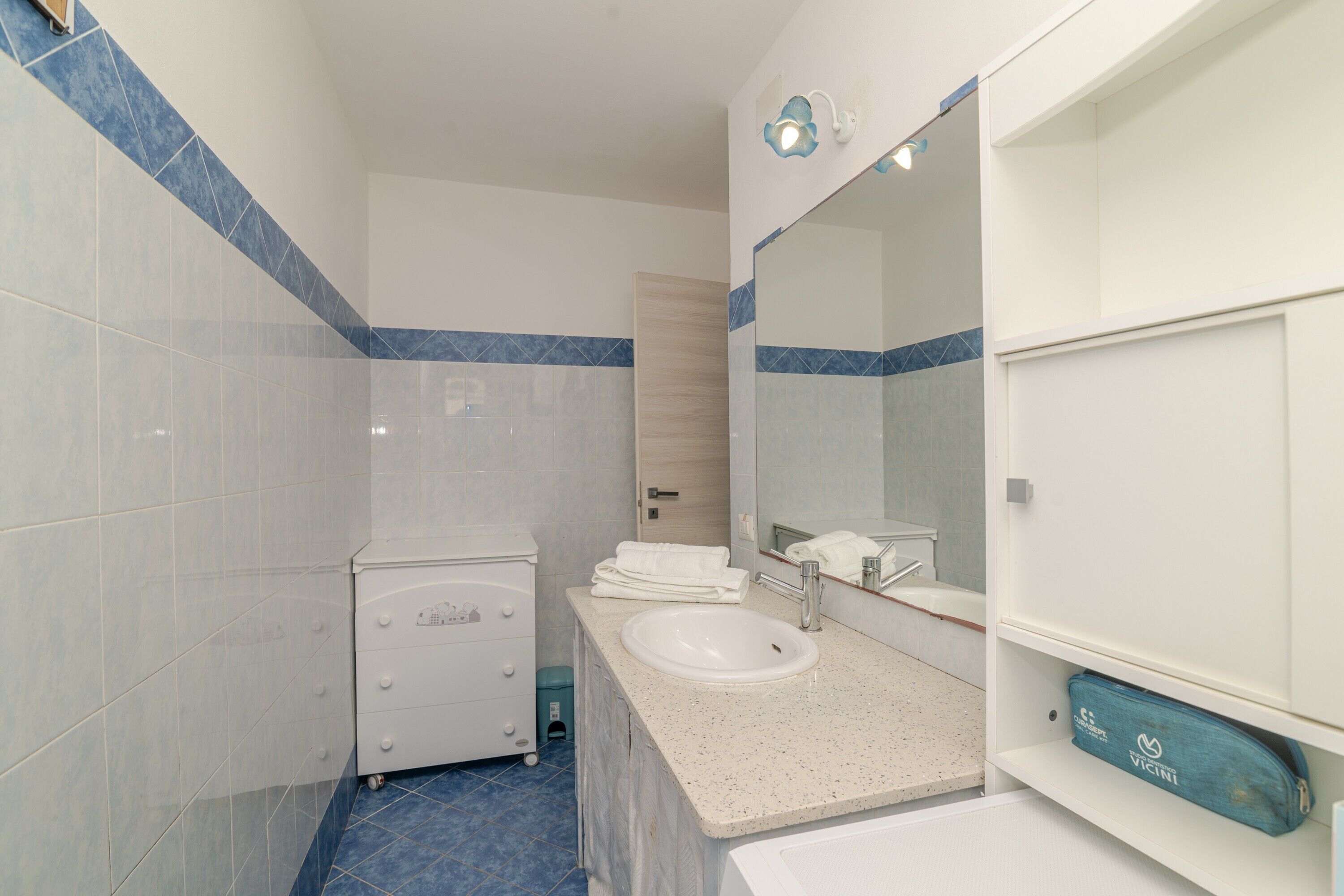Une salle de bain avec un lavabo blanc, un miroir, un meuble blanc et un sol carrelé de bleu.