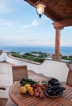 A table with fruits and vegetables, a wooden chair, and a view of the sea. - Relais Maison de Charles (Ischia)