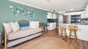Une chambre avec un lit, un bureau et une chaise, une kitchenette équipée d’un réfrigérateur, d’une cuisinière et d’un four à micro-ondes, et un ventilateur de plafond.
