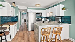 Une cuisine moderne avec des meubles blancs, un îlot central doté de tabourets de bar et une table à manger en bois.