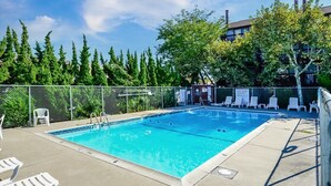 Une piscine rectangulaire avec un escalier, entourée d’une clôture et dotée de chaises longues.