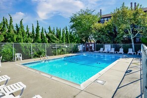 A rectangular swimming pool with a ladder, surrounded by a fence, and equipped with lounge chairs. - Bayfront Condo with Great Views and Nice Amenities (Ocean City)
